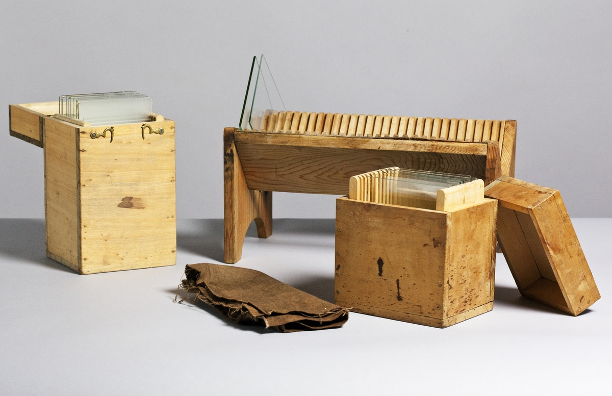 Kamera, skjutlådemodell. Våtplåt 9,5 x 11,5. Objektiv: Alexis Millet, Opticien Bte'SGDG 160r.st:Martin Paris. Nr 605. Utrustning för fotografering på resor, jämte koffert. Lösa delar: kamera av trä med objektiv från Alexis Millet, Paris, nr. 605, objektivlock av mässing, visirskiva, 4 kassetter för våtplåtar 9 x 12 cm, bakstycke med visirskiva för stereobilder 8 x 8 cm, 2 kassetter för stereovåtplåtar, kärl av zinkplåt med lock (gångjärnet avbrutet), trattformat kärl av zinkplåt, mindre kuvert av glas (spräckt och lagad, troligen av givaren), större kuvert av glas, torkställ av trä, 2 skivor av trä med spår för plåtar, kopieram för max 16 x 20 cm, vikbar skiva av trä (för beredning, troligen av våtplåtar), liten bordskiva med kantlist (passar till stativet TM 25.111,fodral av trä med 12 st. våtplåtnegativ 9 x 12 cm (porträtt och skulpturer), fodral av trä med 12 st. sämre negativ, fodral av trä med 10 st. blanka och  skrapade glasplåtar, diverse plåtar i paket (i ask ny 1950), fodral av trä med 11 st. stereovåtplåtar, varav 3 preparerade.
Tillbehör: Koffert.