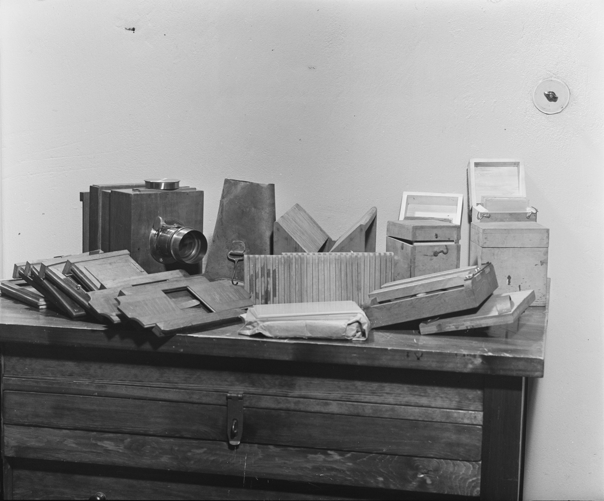 Kamera, skjutlådemodell. Våtplåt 9,5 x 11,5. Objektiv: Alexis Millet, Opticien Bte'SGDG 160r.st:Martin Paris. Nr 605. Utrustning för fotografering på resor, jämte koffert. Lösa delar: kamera av trä med objektiv från Alexis Millet, Paris, nr. 605, objektivlock av mässing, visirskiva, 4 kassetter för våtplåtar 9 x 12 cm, bakstycke med visirskiva för stereobilder 8 x 8 cm, 2 kassetter för stereovåtplåtar, kärl av zinkplåt med lock (gångjärnet avbrutet), trattformat kärl av zinkplåt, mindre kuvert av glas (spräckt och lagad, troligen av givaren), större kuvert av glas, torkställ av trä, 2 skivor av trä med spår för plåtar, kopieram för max 16 x 20 cm, vikbar skiva av trä (för beredning, troligen av våtplåtar), liten bordskiva med kantlist (passar till stativet TM 25.111,fodral av trä med 12 st. våtplåtnegativ 9 x 12 cm (porträtt och skulpturer), fodral av trä med 12 st. sämre negativ, fodral av trä med 10 st. blanka och  skrapade glasplåtar, diverse plåtar i paket (i ask ny 1950), fodral av trä med 11 st. stereovåtplåtar, varav 3 preparerade.
Tillbehör: Koffert.