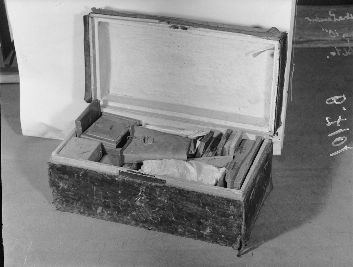 Kamera, skjutlådemodell. Våtplåt 9,5 x 11,5. Objektiv: Alexis Millet, Opticien Bte'SGDG 160r.st:Martin Paris. Nr 605. Utrustning för fotografering på resor, jämte koffert. Lösa delar: kamera av trä med objektiv från Alexis Millet, Paris, nr. 605, objektivlock av mässing, visirskiva, 4 kassetter för våtplåtar 9 x 12 cm, bakstycke med visirskiva för stereobilder 8 x 8 cm, 2 kassetter för stereovåtplåtar, kärl av zinkplåt med lock (gångjärnet avbrutet), trattformat kärl av zinkplåt, mindre kuvert av glas (spräckt och lagad, troligen av givaren), större kuvert av glas, torkställ av trä, 2 skivor av trä med spår för plåtar, kopieram för max 16 x 20 cm, vikbar skiva av trä (för beredning, troligen av våtplåtar), liten bordskiva med kantlist (passar till stativet TM 25.111,fodral av trä med 12 st. våtplåtnegativ 9 x 12 cm (porträtt och skulpturer), fodral av trä med 12 st. sämre negativ, fodral av trä med 10 st. blanka och  skrapade glasplåtar, diverse plåtar i paket (i ask ny 1950), fodral av trä med 11 st. stereovåtplåtar, varav 3 preparerade.
Tillbehör: Koffert.