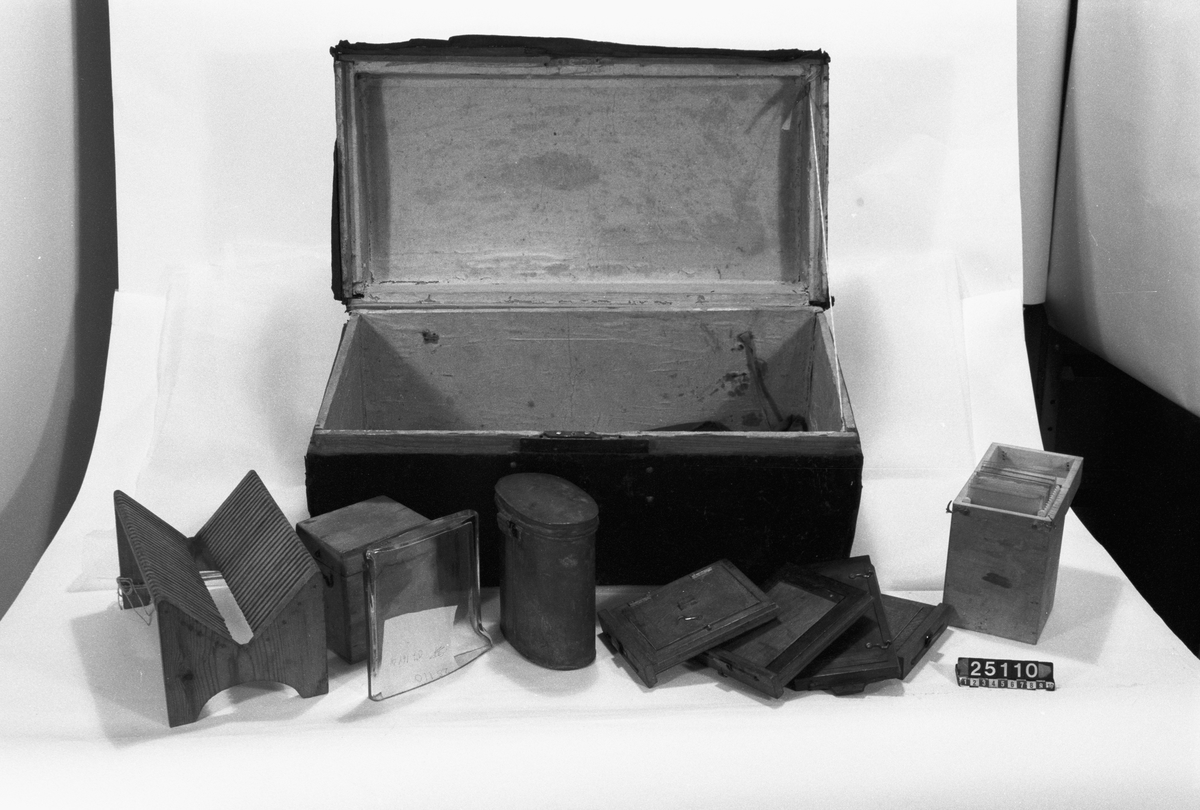 Kamera, skjutlådemodell. Våtplåt 9,5 x 11,5. Objektiv: Alexis Millet, Opticien Bte'SGDG 160r.st:Martin Paris. Nr 605. Utrustning för fotografering på resor, jämte koffert. Lösa delar: kamera av trä med objektiv från Alexis Millet, Paris, nr. 605, objektivlock av mässing, visirskiva, 4 kassetter för våtplåtar 9 x 12 cm, bakstycke med visirskiva för stereobilder 8 x 8 cm, 2 kassetter för stereovåtplåtar, kärl av zinkplåt med lock (gångjärnet avbrutet), trattformat kärl av zinkplåt, mindre kuvert av glas (spräckt och lagad, troligen av givaren), större kuvert av glas, torkställ av trä, 2 skivor av trä med spår för plåtar, kopieram för max 16 x 20 cm, vikbar skiva av trä (för beredning, troligen av våtplåtar), liten bordskiva med kantlist (passar till stativet TM 25.111,fodral av trä med 12 st. våtplåtnegativ 9 x 12 cm (porträtt och skulpturer), fodral av trä med 12 st. sämre negativ, fodral av trä med 10 st. blanka och  skrapade glasplåtar, diverse plåtar i paket (i ask ny 1950), fodral av trä med 11 st. stereovåtplåtar, varav 3 preparerade.
Tillbehör: Koffert.