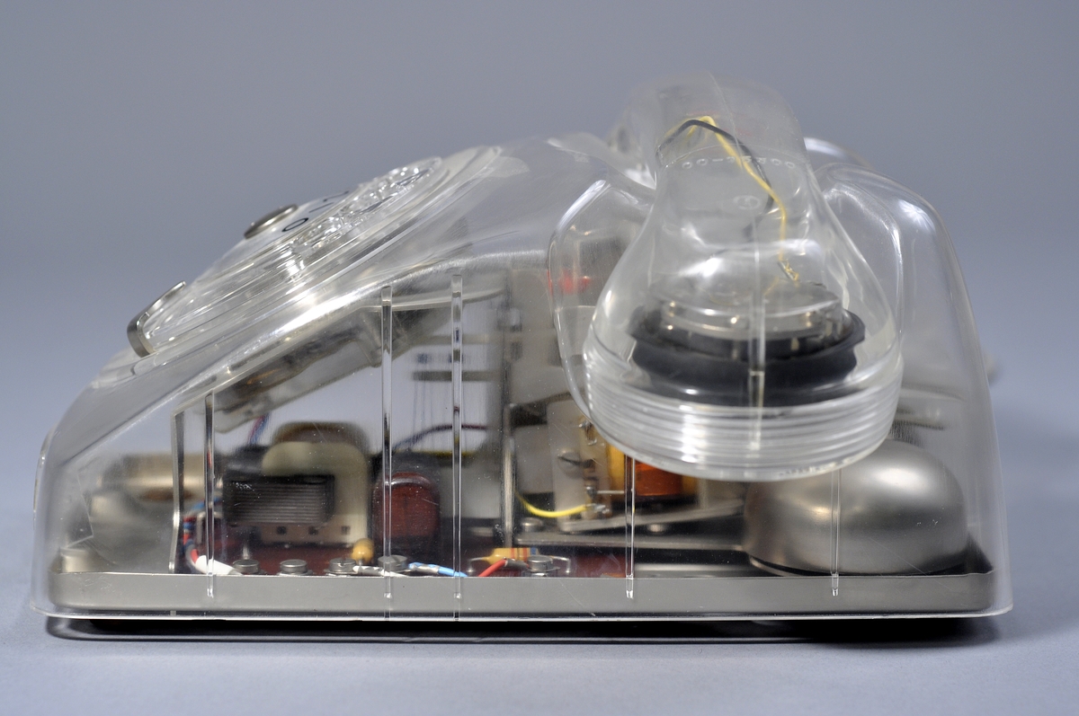 Telefonapparat Dialog för AT-system, huvudapparat, anknytningsapparat till växel och sidoapparat. Bordsmodell av genomskinlig termoplast med fingerskiva. Ringsignalens styrka är ställbar med ett reglage på apparatens undersida.