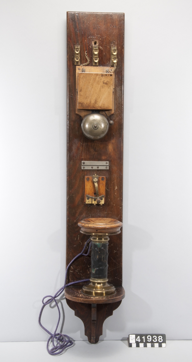 Telefonapparat med galvanisk klocka, magnettelefon, vevomkastare och åskskydd, väggmonterad på bräda, med hörtelefonerna förväxlade. Lokalbatteri.