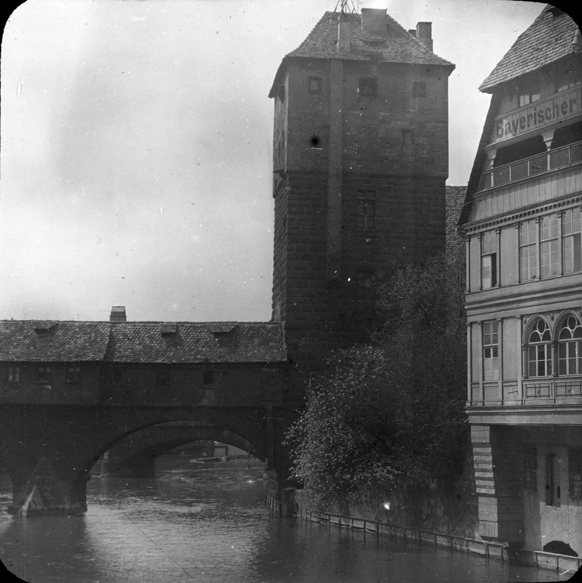 Skioptikonbild med motiv av Henkersbrücke vid floden Pegnitz med vattentornet till höger. Weinstadel ligger bakom tornet. Fleischerbrücke ligger österut, Nürnberg.
Bilden har förvarats i kartong märkt: Nürnberg. III.. Text på bild: "Nürnberg 1901"