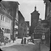 Skioptikonbild med motiv av torget Plönlein vid gatorna Kobolzellersteig och Spitalgasse.
Bilden har förvarats i kartong märkt: Rothenburg IV.