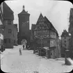 Skioptikonbild med motiv av torget Plönlein vid gatorna Kobolzellersteig och Spitalgasse.
Bilden har förvarats i kartong märkt: Rothenburg IV. Text på bild: 