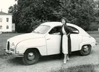 Kvinna poserar framför Saab- 93, för fyra passargerare.