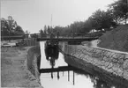 Kinda kanal. Slussbron vid Slattefors. Bakom bron synd båten Sigfrid från Stockholm.
Med fotografiet erhöll fotografen 5:e plats i Svenska Turistföreningens pristävlan 1902.