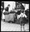 Skioptikonbild från institutionen för fotografi vid Kungliga Tekniska Högskolan. Använd av professor Helmer Bäckström som undervisningsmaterial. Bäckström var Sveriges förste professor i fotografi vid Kungliga Tekniska Högskolan 1948-1958. Bilden föreställer torghandel i Nürnberg. Bilden är beskuren. Se bild SKC6178 och SKC6179.