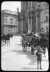 Skioptikonbild från institutionen för fotografi vid Kungliga Tekniska Högskolan. Bilden är troligen tagen av John Hertzberg under en resa i Europa. Hertzberg blev docent i fotografi 1921vid Kungliga Tekniska Högskolan i Stockholm. Hästdroskor utanför katdralen i Syrakusa.