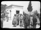 Skioptikonbild från institutionen för fotografi vid Kungliga Tekniska Högskolan. Motiv föreställande sällskap utanför ett mausoleum, sannolikt i södra Italien. Bilden är troligen tagen av John Hertzberg under en resa i Europa..