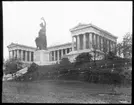 Skioptikonbild från institutionen för fotografi vid Kungliga Tekniska Högskolan. Motiv föreställande monumental byggnad med skulptur framför föreställande en kvinnogestalt som håller en lagerkrans i handen och med ett lejon vid sin sida. Bilden är troligen tagen av John Hertzberg under en resa i Europa.