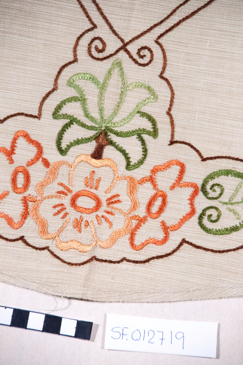 Oval, brodert duk, blomemotiv. Sydd plattsaum og stilkesting.