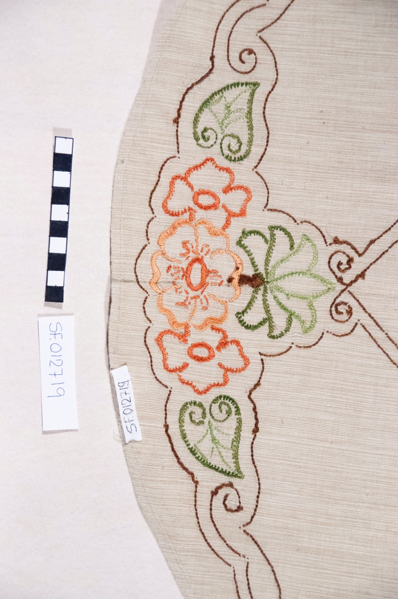Oval, brodert duk, blomemotiv. Sydd plattsaum og stilkesting.