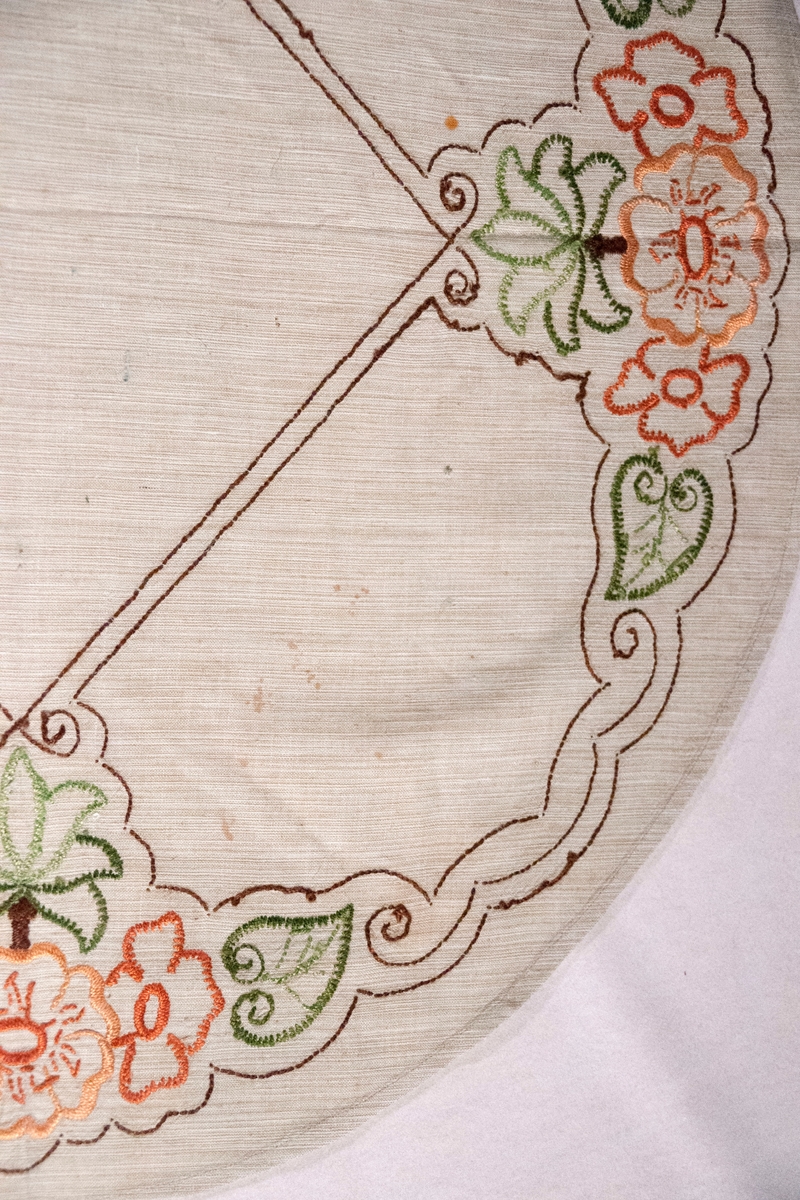 Oval, brodert duk, blomemotiv. Sydd plattsaum og stilkesting.