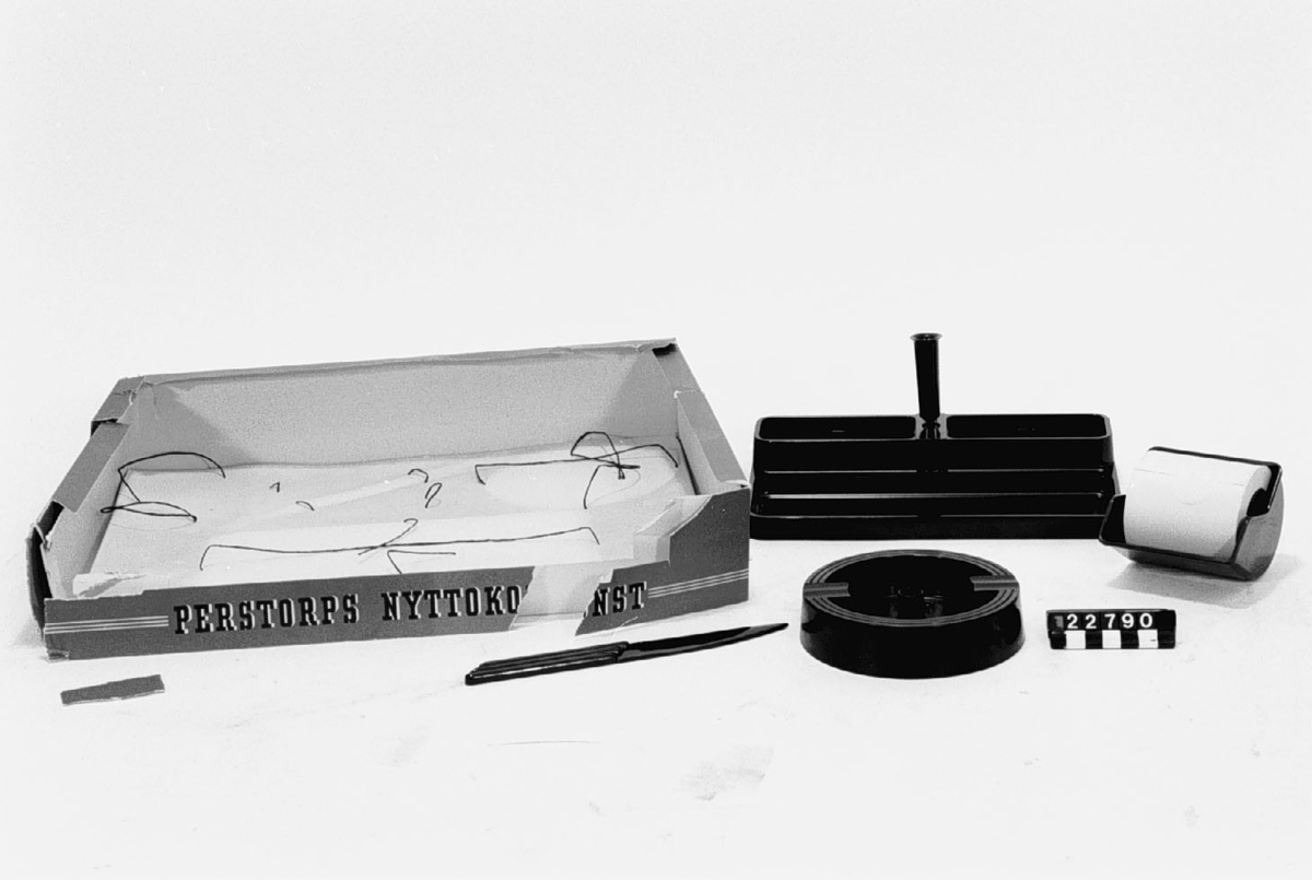 Skrivbordsats av isolit, konstharts. Bestående av: pennfat med fack för små föremål och pennhållare, vridbar i kulled, läskdabb#,papperskniv och askkopp. I originalkartong för reklam för "Perstorps Nyttokonst".