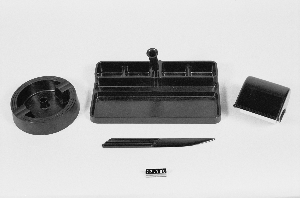 Skrivbordsats av isolit, konstharts. Bestående av: pennfat med fack för små föremål och pennhållare, vridbar i kulled, läskdabb#,papperskniv och askkopp. I originalkartong för reklam för "Perstorps Nyttokonst".
