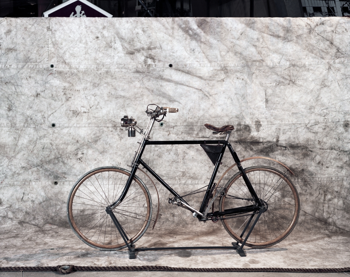 Herrcykel av typ upp-och-nertrampare (till skillnad från rundtrampare). Upp-och-nedgående pedaler med kedjor till baknavet som är en s.k. rullspärr enl. Birger Ljungströms konstruktion, patenterad 1892. Rullspärren ger frihjulsfunktion. De fram-och-återgående kedjorna ger baknavet en roterande rörelse genom två excentriska "drivskivor". Fem tryckluftsreglerade växlar. På styret finns två gummiblåsor dolda under metallhöjle. Luften leds med slangarna till ytterliggare två gummiblåsor placerade på segmenten vid tramporna. Broms på bakhjulet genom att de båda tramporna trycks ned och påverkar en hävarm som trycker två roterande koniska bromsklotsar mot bakdäcket. Senare modell hade s.k. skedbroms mot bakdäcket. Framhjulsbroms med s.k. skedbroms mot framdäcket. Fälgar och skärmar av trä.
Tillbehör: Verktygsväska, signalklocka, skylt med polisens ordningsnr, 6808.