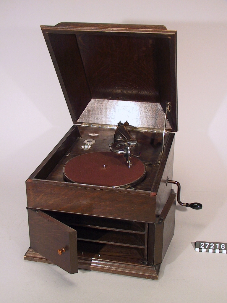 Grammofon, bordsapparat av trä med inbyggd ljudtratt och dörrar för ljudöppningen. Under lådan etikett: "110 Registered Design Rd. No 605812". Originalljuddosa "His master's voice" nr 2. Anordning för automatiskt stopp, när skivan är utspelad.