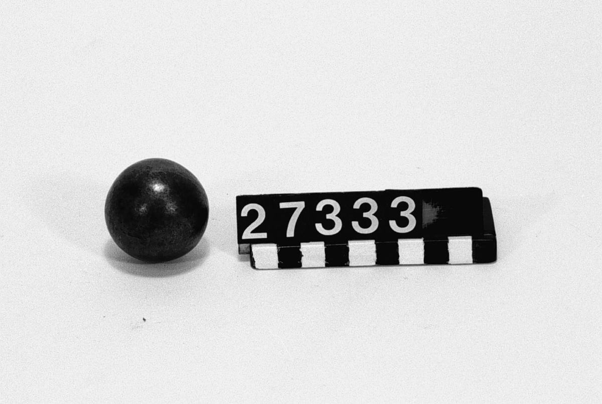 Ihålig kula av järn med klangeffekt, smidd genom hetsning utan synlig skarv. Mästerstycke av kinesisk bysmedskonst. Kulan väger ca. 215 g. Om klangen (av malm eller silver?) och kläppen (en kula?) väger 15 g. så är kulans vägg ca. 6.05 mm tjock vid specifik vikt 7.8 kg. Inre diameter 30 mm. I ask.