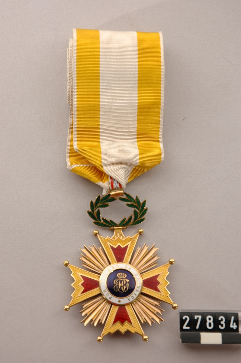Kommendörstecken av 3:e klass av spanska Isabel la Catolica orden, i band av siden, gult-vitt-gult, överlämnat till John Ericsson. Åtsidan: 4-armat malteserkors, strålar emellan, guld- och rubinemalj, kungligt namnchiffer i guld på blå emalj, runtom i guld på vitt: "Por Isabel la Catolica". Frånsidan: Två stympade kolonner, två bundna blå klot, runtom: "A la leated acrisolada".
