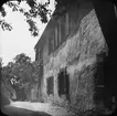 Skioptikonbild med motiv av flicka vid gamalt hus i Rothenburg.
Bilden har förvarats i kartong märkt: Vårresan 1910. Rothenburg. XXX.