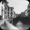 Skioptikonbild med motiv av gata vid flod i Granada.
Bilden har förvarats i kartong märkt: Höstresan 1910. Granada 9. N:24. Text på bild: 