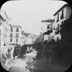 Skioptikonbild med motiv av gata vid flod i Granada.
Bilden har förvarats i kartong märkt: Höstresan 1910. Granada 9. N:24