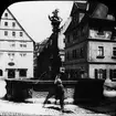 Skioptikonbild med motiv av man vid fontän i Rothenburg.
Bilden har förvarats i kartong märkt: Vårresan 1910. Rothenburg. XXVII. Text på bild: 