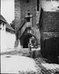 Skioptikonbild med motiv av liten flicka vid tornet Jörgentor i stadsmuren, Münnerstadt.
Bilden har förvarats i kartong märkt: Vårresan 1910. Münnerstadt 9. VII.