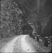 Skioptikonbild med motiv av bil på väg in i tunnel  längs väg i dalgången Finstermünz, på gränsen mellan Österrike och Schweiz.
Bilden har förvarats i kartong märkt: Resan 1909. Finstermünz. N:26.