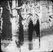 Skioptikonbild med motiv av pojke vid staket utanför Cathédrale Notre-Dame d'Louviers.
Bilden har förvarats i kartong märkt: Resan N:2. 1908.Evreux 5. Louviers 5. I. Text på bild: 