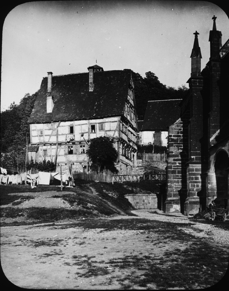 Skioptikonbild med motiv av hus intill Stiftskirche i Herrenberg.
Bilden har förvarats i kartong märkt: Resan 1908. Herrenberg.