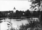 Diapostiv, fönsterbild med motiv från Husby kyrka, sommarlandskap. Vy över älv. Man i eka (roddbåt) med kyrka i bakgrunden.