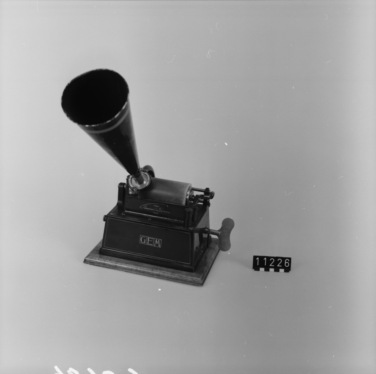 Fonograf, enligt Edison. Mindre typ, fjäderverksdriven, jämte "recorder" för upptagning. Recorderns nr. 10882. Monterad på träplatta. Skyddshuv med handtag.