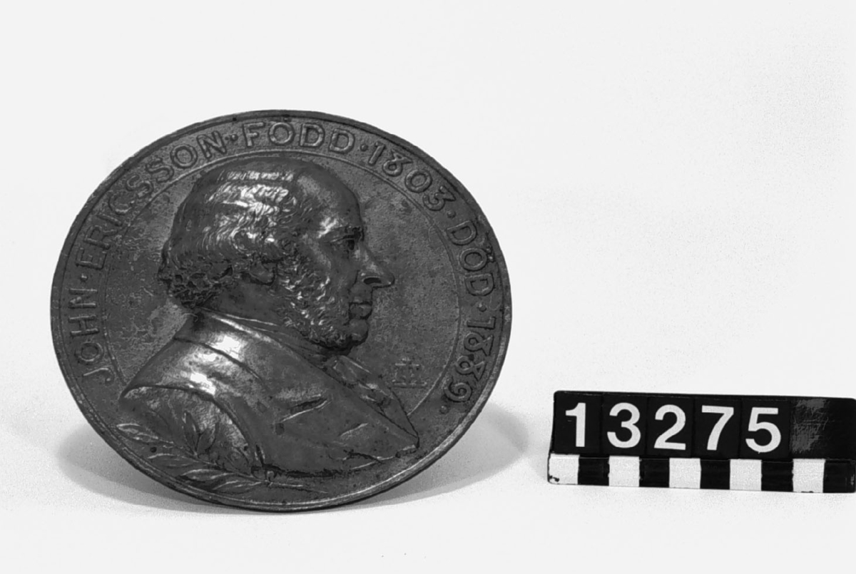 Medaljong, gjuten i brons, över John Ericsson, höger profil, signerad LA. "John Ericsson född 1803 död 1889".