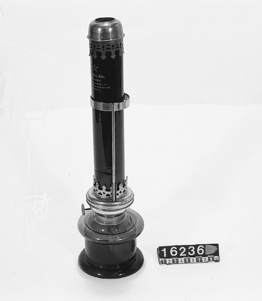 Lampa för fotografiskt mörkrum, för fotogen med yttre lampglas av rubinfärgat glas. Text på glaset: "Ica Akt.-Ges. Dresden, Spektroskopisch für Photographie lichtsicher befunden",
Tillbehör: Lampa, yttre lampglas samt huv till lampglaset.