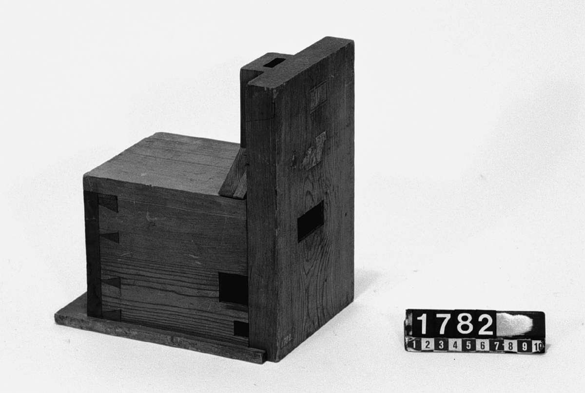 Modell av bakugn. Text på föremålet: "D. (?)". I Jonas Norbergs förteckning från 1779 beskrivs modellen på följande sätt: " Modell på Spisell, med bakugn och torkställe der ofvanuppå, inventerad af Undertecknad [J. Norberg] til tarflige hushålls behof, der man efter landtmaner, har bakugnen inne uti boningsrummet# denne bakugn har sin särskilte eldningsugn, hvarifrån värmen går både under och öfver bakugnen, så att denna senare aldrig behöfver sopas, utan kan oafbrutit nyttjas til brödets bakning. Spiseln är gjord som en liten kjöksspis, hvarifrån då kokningen är skedd, den öfrige elden skyflas in i eldningsugnen, at der brinna ut, lika som i en kakelugn. Men då man intet behöfver koka, utan eldar blott för at värma rummet, då lägges veden straxt in uti eldningsugnen, hvars öppning är inuti spisen, hvarifrån värmen dunstar in uti rummet vid bakugnen hvilkens mynningar är på ena sidan om spisen."