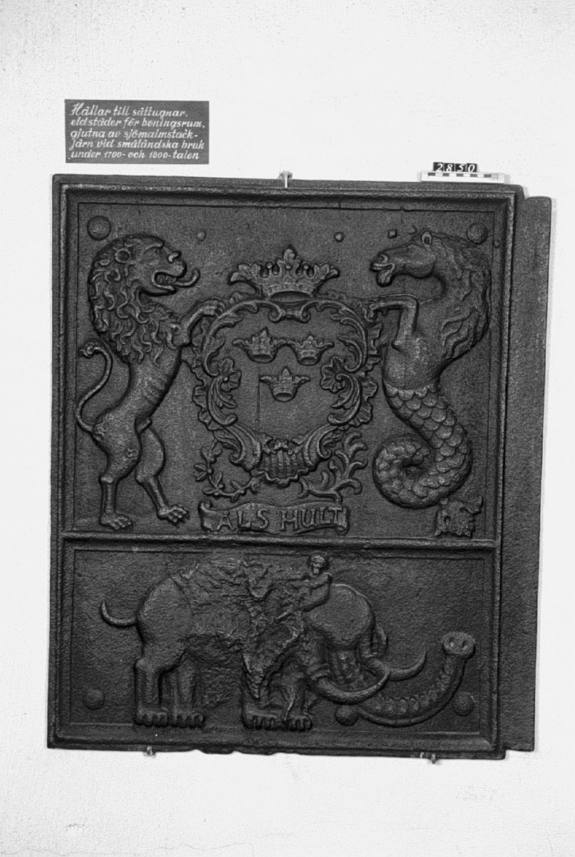 Sidohäll till sättugn, av gjutjärn. I mitten vapen med tre kronor buret till vänster av ett lejon till höger av en sjöhäst. Nedre hällen, en elefant. I randkartusch: "Åls Hult".