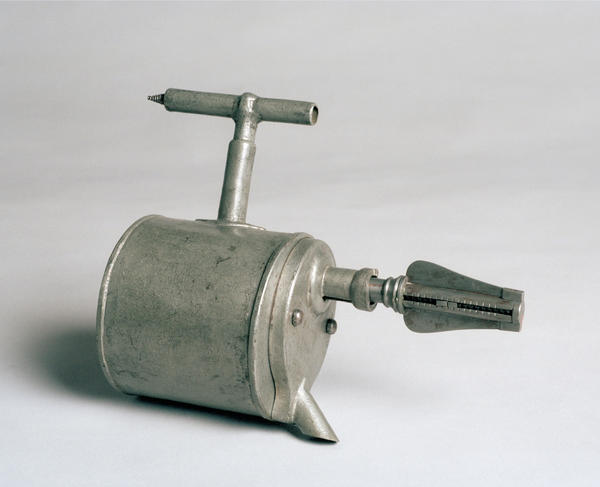 Christopher Polhem's strange tap, made of tinplate with the fixed parts riveted and soldered. The gear and its sleeve, the sleeve on the pipe and a liner in the drain of the container are made of brass. The tap is to be mounted in the barrel. The amount of liquid that is drawn out is portioned with a key. It also functioned as a lock and limited access to the barrel's contents. This specimen was probably exhibited at the 1866 exhibition in Stockholm, by "Stiernsunds Bruksegare", according to a contemporary exhibition catalogue.