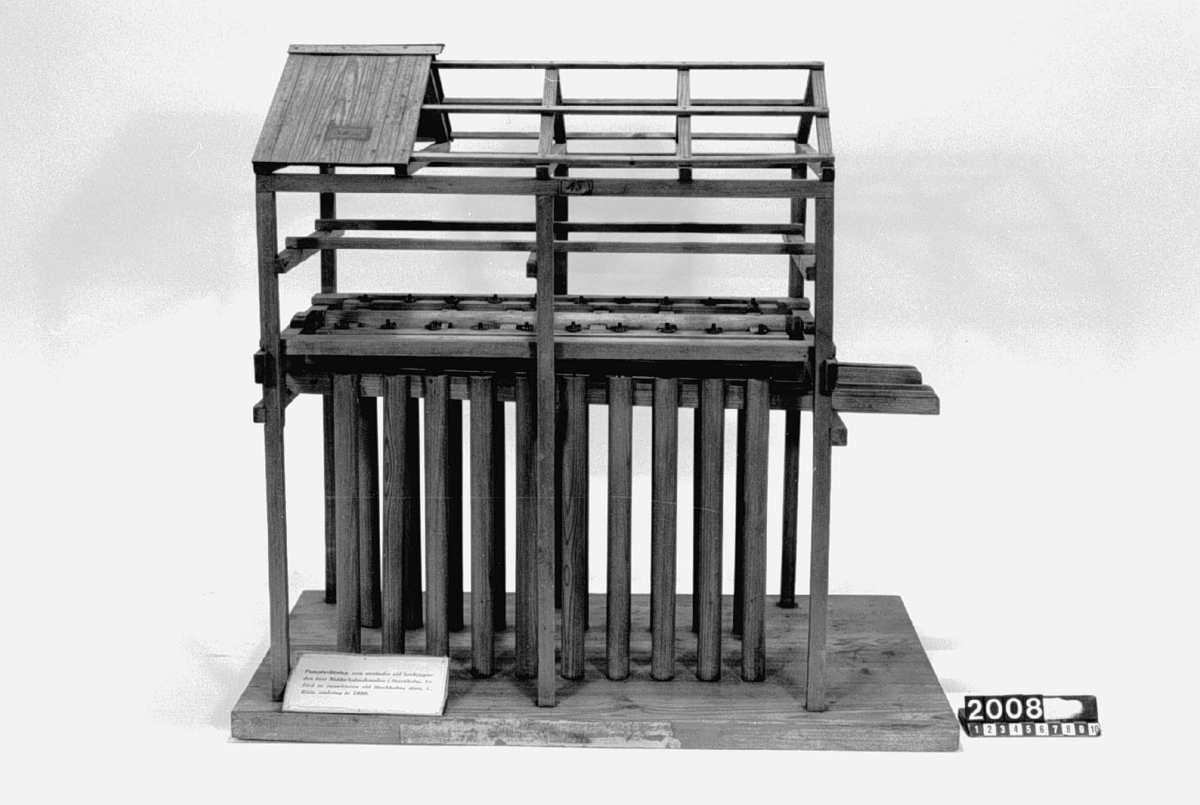 Modell av pumpinrättning. Text på föremålet: "Modell på Pump Invention, som bruktes i Riddarholms Canalen wid den ... brobyggnaden. Af Inspectorn wid Stockholms Sluss Herr C. Röös" text på skilt.