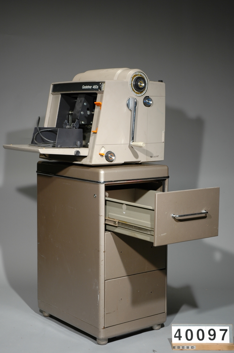 Stencilapparat, Gestetner 460s, 200W. 46kg. L 425mm B 490 H 450 Skåp av metall för div. tillbehör med tre lådor, Mått: 410bx590lx800h, vikt inkl innehåll: 54 kg. Innehåll: 7 st paket stenciler, 17 st tuber grå färg och rengöringsvätskor 1st instuktionsbok för Stencilerings apparat Gestetner 466. Ca 150st påbörjade stenciler m text "Tonårsbrevet" Skåp av plywood vari man förvarade färdiga och infärgade stenciler, grått, tomt. 8kg Bredd: 570 mm, längd: 175 mm, höjd: 573 mm. Brännare, Gestetner 473, No F92426, 200W, tysk, ljusbrun plast. vikt 23kg Bredd: 390 mm, längd: 690 mm, höjd: 225 mm.