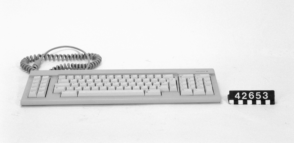 Tangentbord till persondator av beige plast. QWERTY-layout med svenska tecken. Funktionstangeter och numerisk del. Spiralsladd med DIN-kontakt för anslutning till dator.