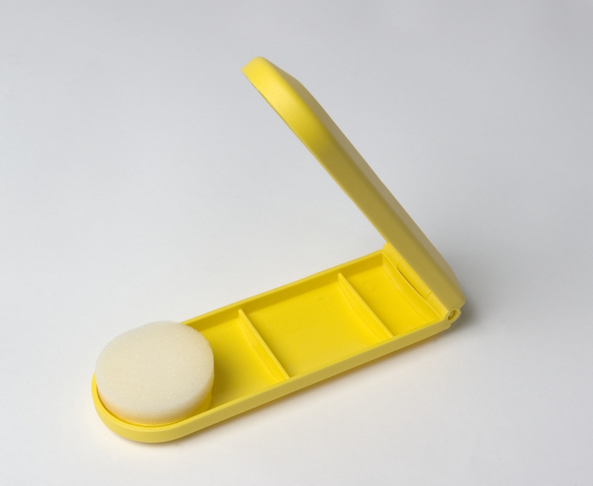 Applikationsbox för hudkräm som kan fällas ut. En skumgummirondell fästs på applikatorn som i utfällt läge fungerar som en förlängd arm och gör att man till exempel lättare kan smörja in sig på ryggen utan hjälp. Man slipper också bli kladdig om fingrarna.