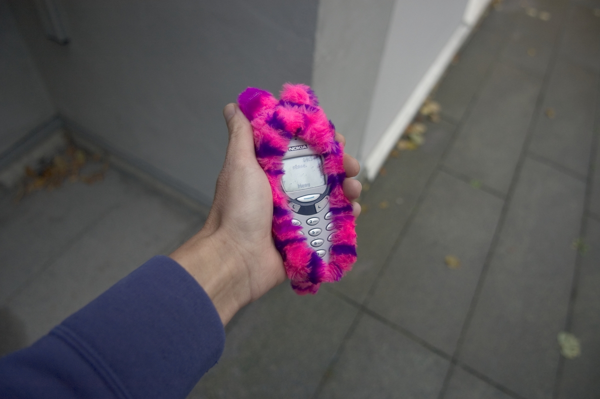 Mobiltelefonfodral i syntetpälsmaterial. Skall skydda mobilen från stötar och göra mobilen behagligare att använda när det är kallt ute.