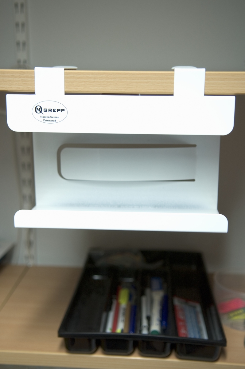 Hållare för förpackningar med engångshandskar. Hållaren passar de flesta typer av engångshandskar i 100-pack som används inom vård och omsorg, restaurang, storkök m.m. Hållaren kläms fast under en hylla