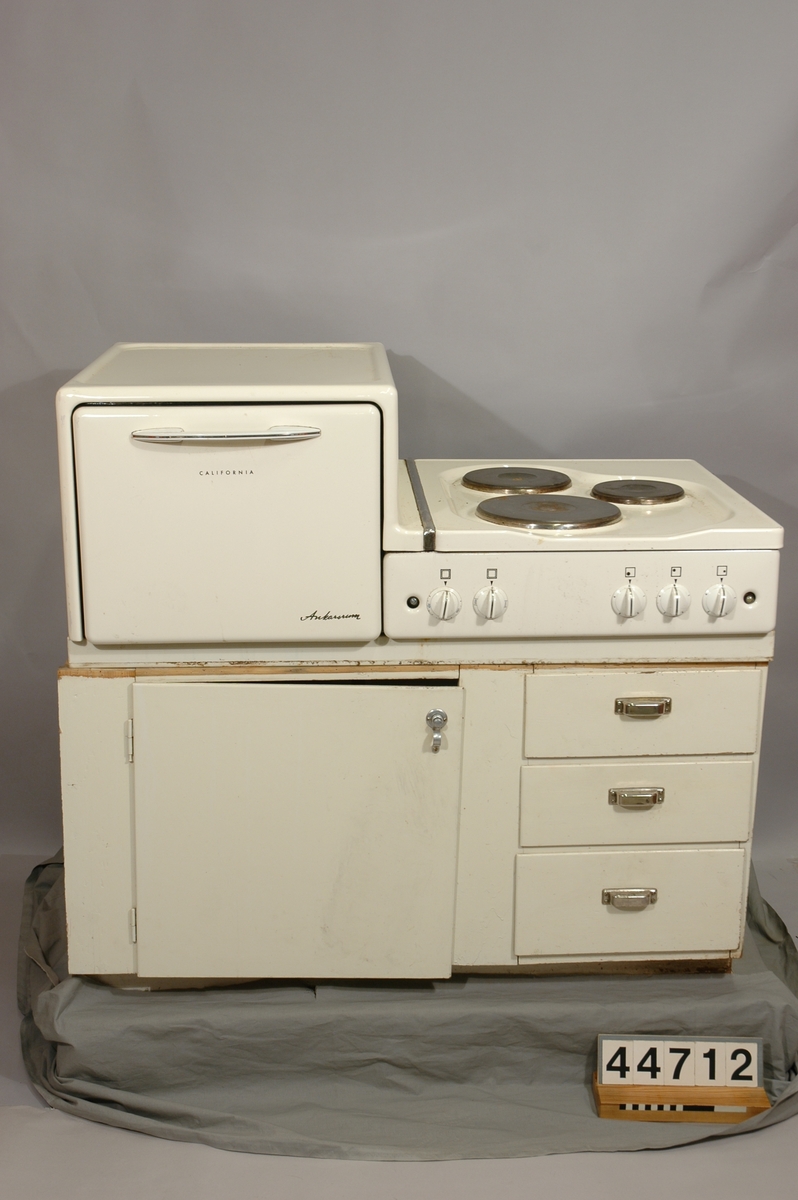 Elektrisk spis med tre kokplattor och vidstående ugn, på underrede i form av bänkskåp med luckor och lådor. Avsedd för 220 V växelström, 5600 W effekt. Emaljerad i beige nyans, ugnen grön invändigt. Två bakplåtar medföljer.  Spisens mått exkl underskåp l=680, b=1094, h=435.