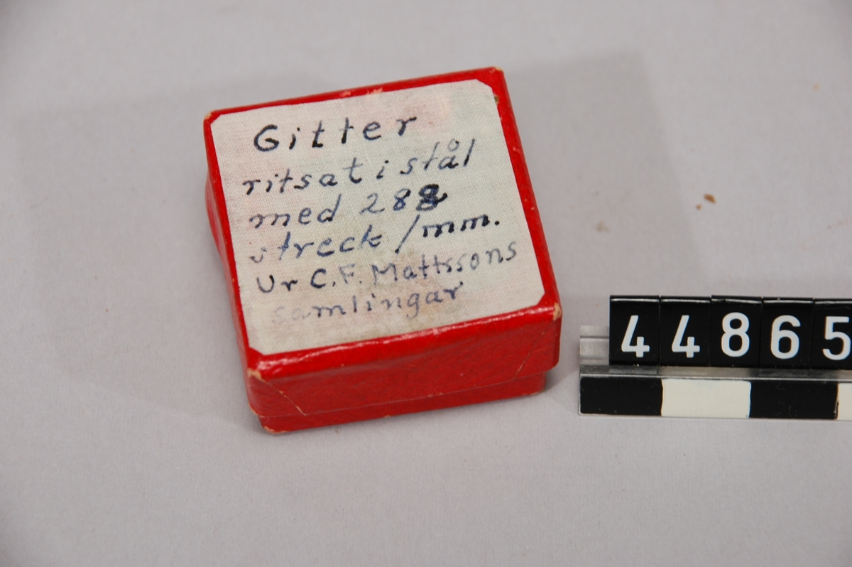 Stålstycke med gitter, i rött pappetui med text: Gittret ritsat i stålet med 282 streck/mm. Gitter är ett optiskt element med mycket nära liggande väldigt smala linjer.