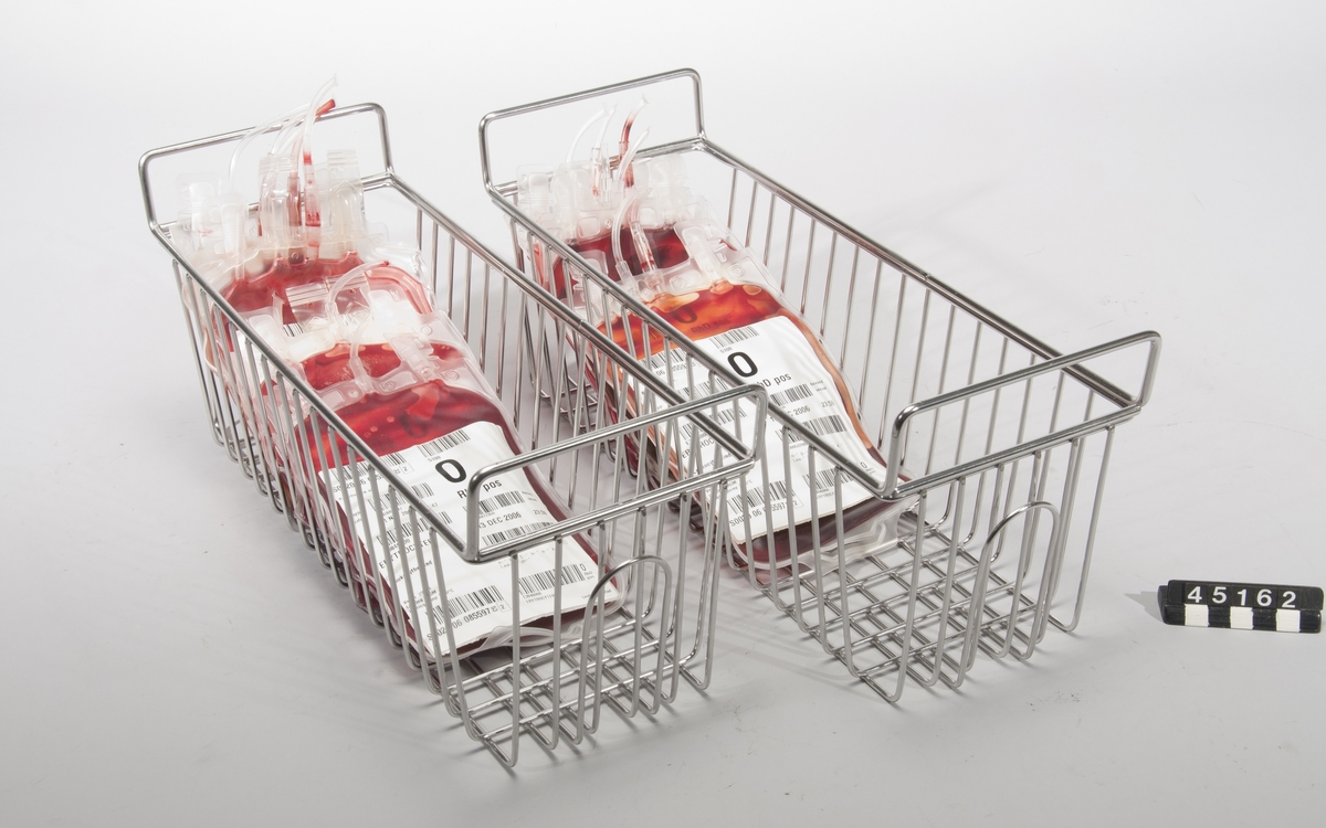 Korg för blodpåsar, två st, i rostfritt stål. Avsedd för förvaring av blod till transfusione, vilket måste förvaras svalt. En korg rymmer 10-12 blodpåsar. Korgen är lätt att hantera och kan lätt rengöras och steriliseras.  Till föremålet finns påsar med röd vätska som rekvisita.