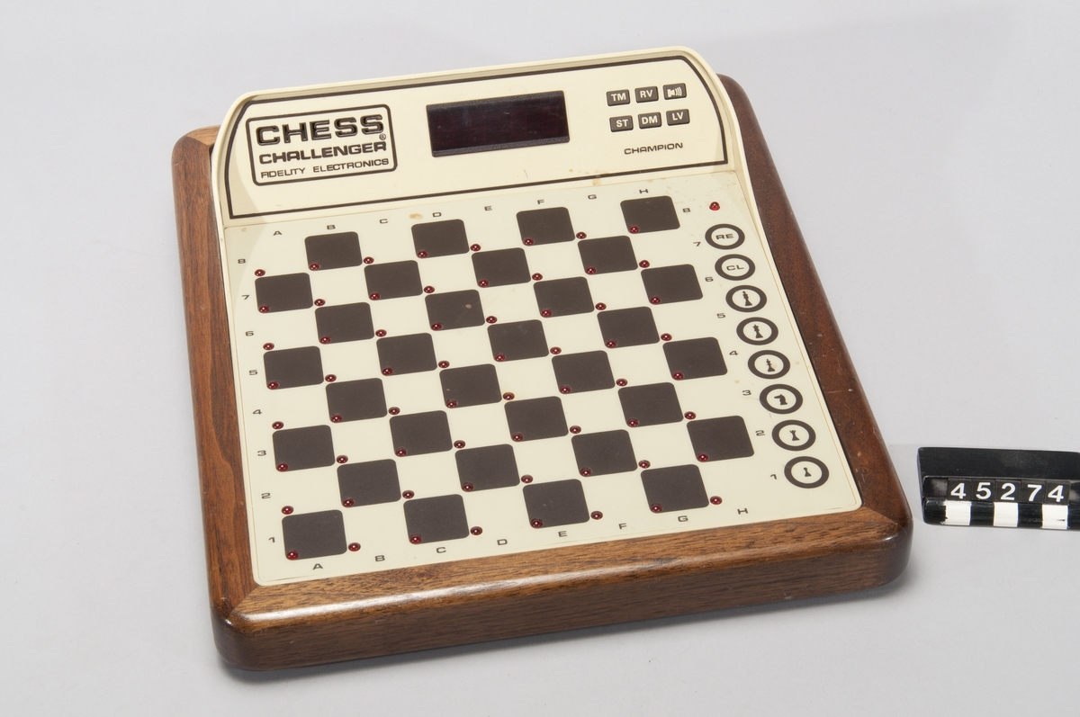 Schackautomat, Fidelity Chess Challenger Champion. Spelet ställs upp med svarta pjäser i övre ändan, mot displayen. Vid korrekt uppställning står vit kung på E1, svart på E8. Om man väljer att spela passivt ska vit kung stå på D8 och svart på D1. Genom att trycka ned spelarens kung (innan andra pjäser flyttas) går det att ställa in svårighetsgrad. Automaten registrerar sedan spelarens drag och gör egna, men spelaren måste flytta båda sidors pjäser. När automaten ställer spelaren i schack matt säger den det, också om mattdraget är oundvikligt: "Check and mate in 3".  Åtta bitars processor, MOS tech. typ 6502, 16 kB ROM, 4 kB RAM. Shackdatorn har 12 svårighetsnivåer. Den har även sensorisk röst som är datorgenererad och uttalar dragen. Det finns femtio ord i minnet, för att beskriva t ex vilken pjäs som flyttas eller om kungen står i schack. Den kan också bekräfta pjäsernas placering på brädet, på begäran av användaren.  Schackautomaten saknade vid förvärvet originalpjäserna. Patent 4.235.442