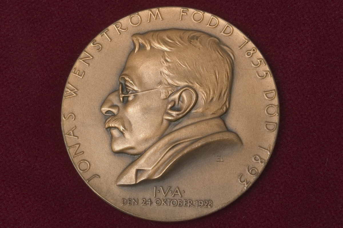 Medalj i brons över Jonas Wenström född 1855, död 1893. Tjocklek: 4 mm. Åtsidan: Porträtt i lågrelief vänster profil av J. Wenström och "JONAS WENSTRÖM FÖDD 1855 DÖD 1893". Text i nedre kanten: "I.V.A. DEN 24 OKTOBER 1928". Frånsidan: Prometheusfigur. Signerad: Erik Lindberg.